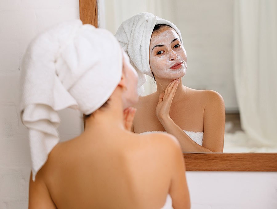 Mujer se pone crema en toda la cara delante del espejo.